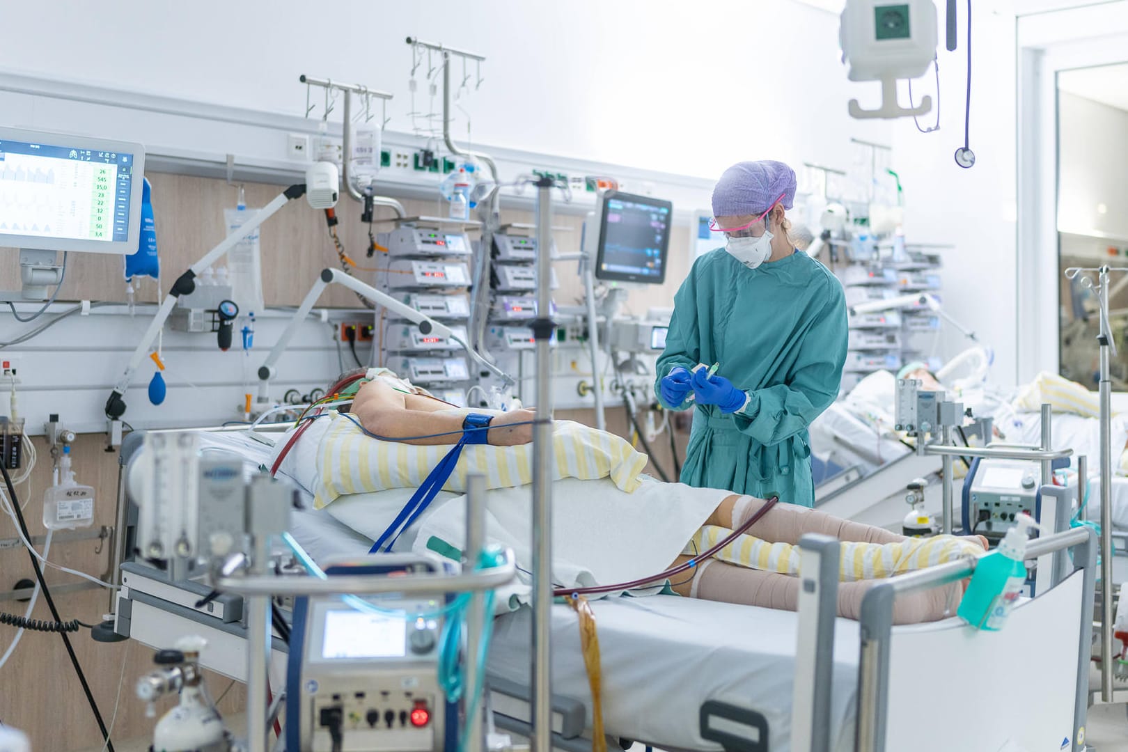 Ein Pfleger auf einer Corona-Intensivstation steht am Bett eines Patienten. Die Corona-Neuinfektionen steigen weiter.