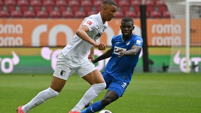 Augsburgs Abwehrspieler Felix Uduokhai (l) behauptet sich gegen Hoffenheims Stürmer Ihlas Bebou.