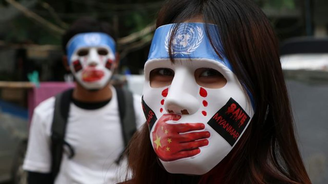 Junge Demonstranten in Yangon tragen Masken, auf denen das Logo der Vereinten Nationen, eine rote Hand über dem Mund, rote Tränen und Aufkleber mit der Aufschrift "Save Myanmar" zu sehen sind.