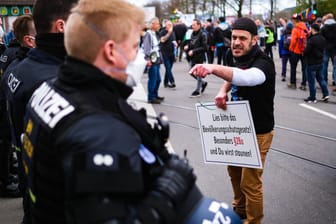 Ein Teilnehmer der "Querdenken"-Proteste in Stuttgart diskutiert mit der Polizei - ohne Mundschutz: Journalisten und Politiker kritisieren, dass die Polizei die Versammlung nicht aufgelöst hat.
