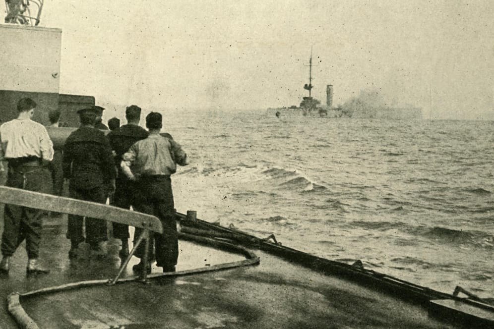 Das deutsche Kriegsschiff "SMS Mainz" (im Hintergrund) versinkt im Sommer 1914: Nun wollen Forscher herausfinden, wie gefährlich die sich zersetzenden Weltkriegswaffen für die Umwelt sind.