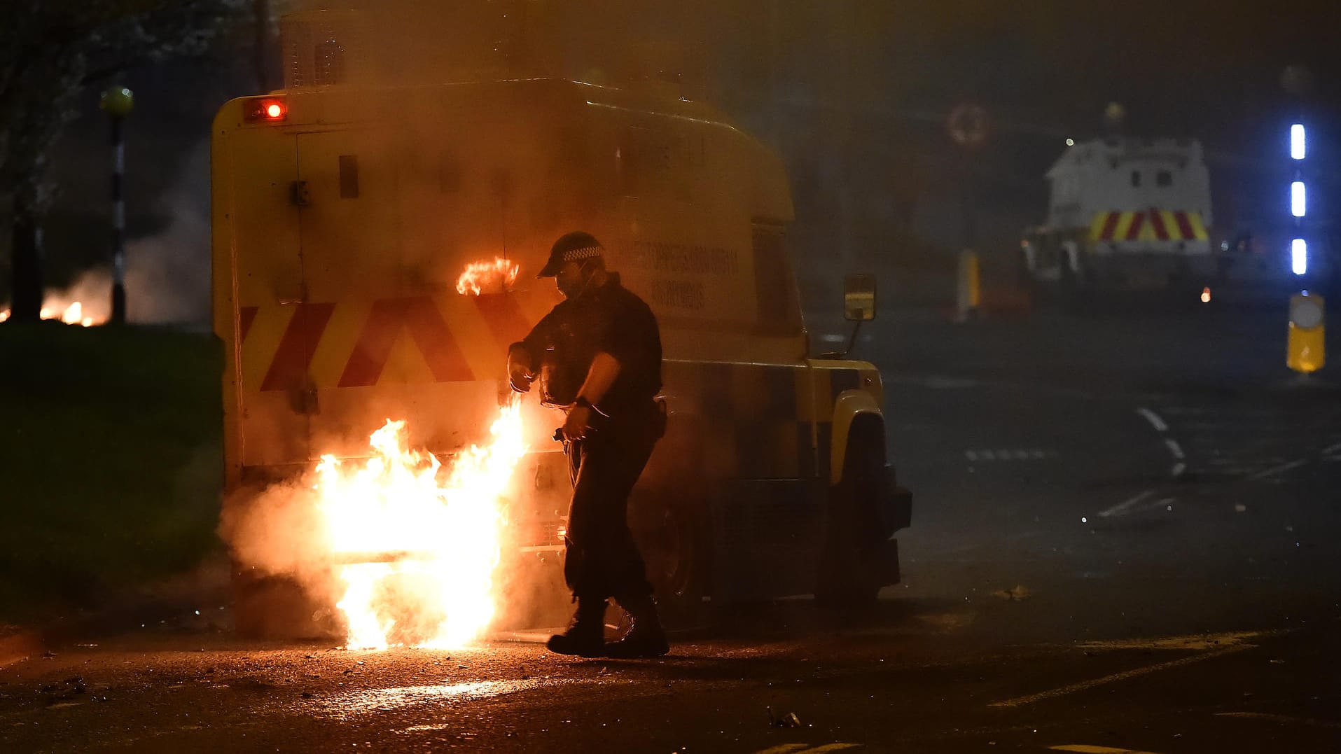 Ein Polizist löscht am Samstag in Cloughfern einen brennenden Wagen: Die Krawalle halten weiter an.