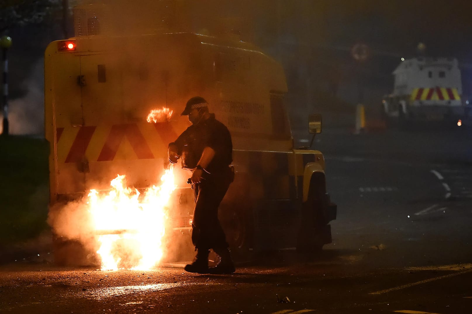 Ein Polizist löscht am Samstag in Cloughfern einen brennenden Wagen: Die Krawalle halten weiter an.