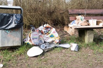 Müll liegt neben einem Mülleimer und auf einer Parkbank (Symbolbild): Besonders an warmen Tagen kämpft die Stadt mit großen Müllmengen.