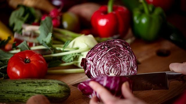 Eine Frau schneidet auf einem Schneidbrett mit einem Küchenmesser einen Radicchio. Eine Frau schneidet auf einem Schneidbrett mit einem Küchenmesser einen Radicchio.