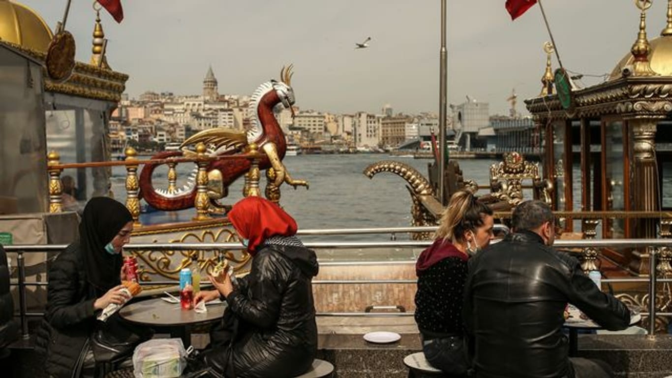 Menschen essen an Tischen am Ufer vom Goldenen Horn auf dem Eminonu Markt in Istanbul.