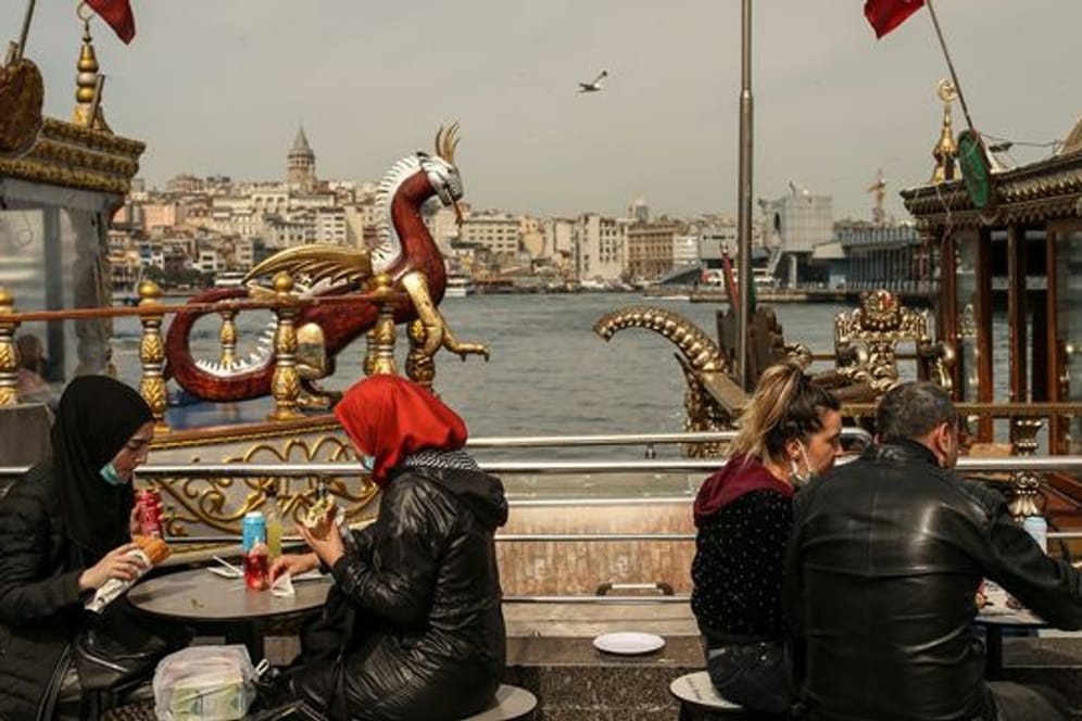 Menschen essen an Tischen am Ufer vom Goldenen Horn auf dem Eminonu Markt in Istanbul.