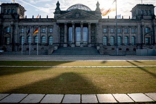 Die Sonne steht am Morgen hinter dem Reichstagsgebäude mit dem Bundestag.