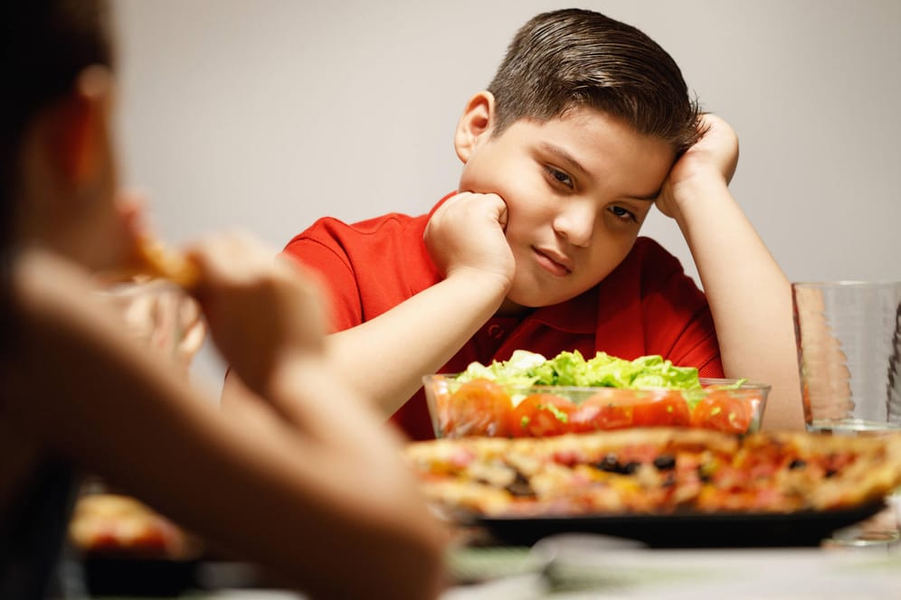 Ein trauriges Kind sitzt vor dem Essen (Symbolbild): Die Corona-Pandemie hat laut Experten massive Auswirkungen auf Kinder.
