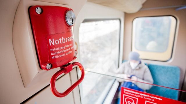 Ein Fahrgast mit Mund-Nasen-Schutz sitzt in einer Berliner S-Bahn hinter der Notbremse. Ein Fahrgast mit Mund-Nasen-Schutz sitzt in einer Berliner S-Bahn hinter der Notbremse.