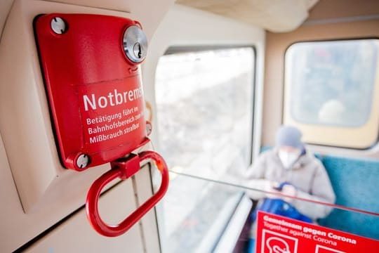 Ein Fahrgast mit Mund-Nasen-Schutz sitzt in einer Berliner S-Bahn hinter der Notbremse.