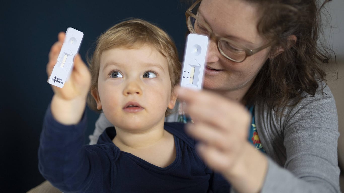 Eine Frau und ein Kind halten einen Corona-Schnelltest hoch (Symbolbild): Die Eltern sollen ihre Kinder zwei mal wöchentlich auf das Coronavirus testen.