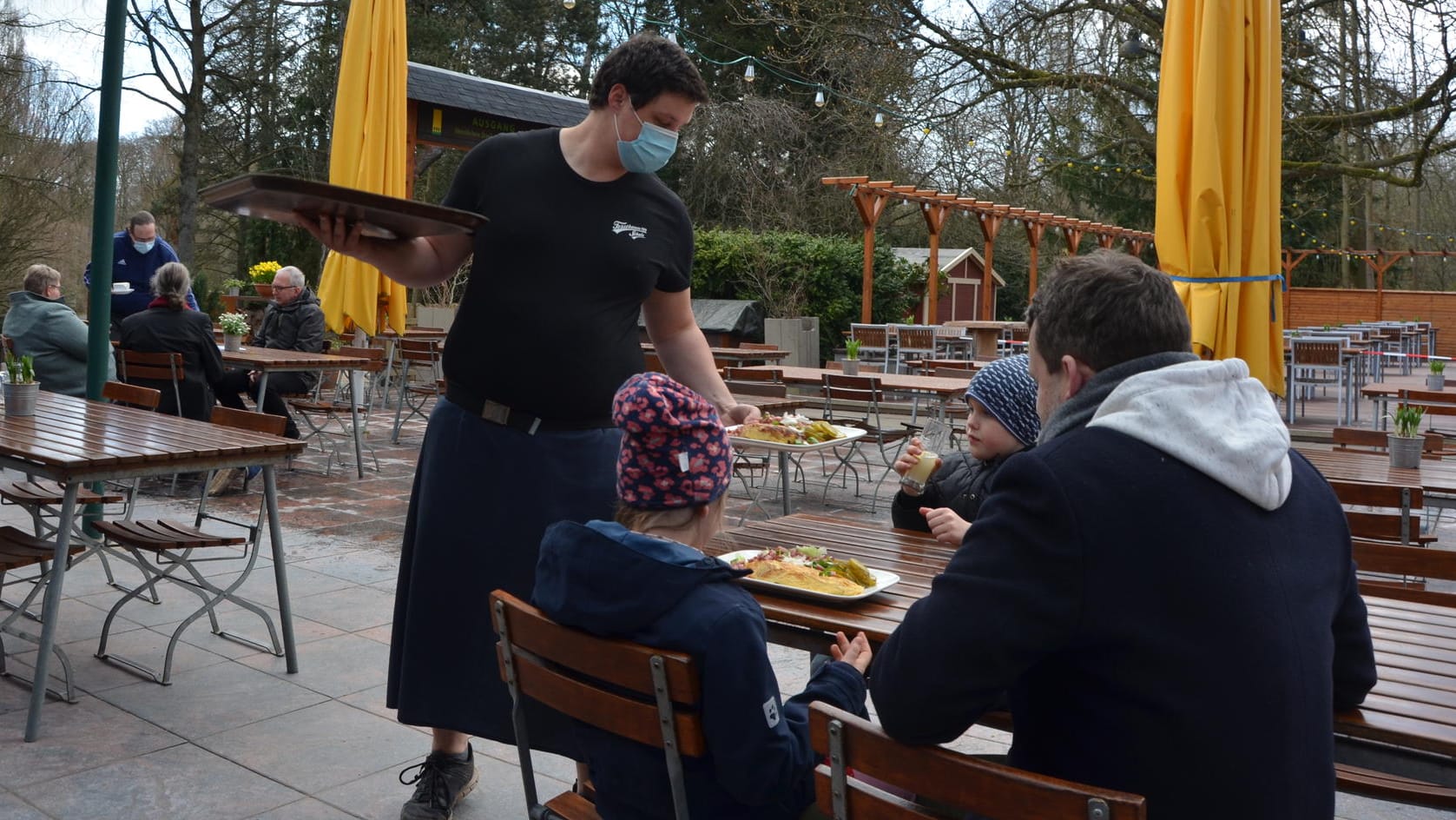 In der Forstbaumschule bedient ein Kellner Gäste: In dem Außenbereichs des Restaurants haben normalerweise 250 Gäste Platz, wegen Corona dürfen nun nur noch bis zu 90 kommen. Dich am ersten Tag der Öffnung kam noch weniger Gäste.