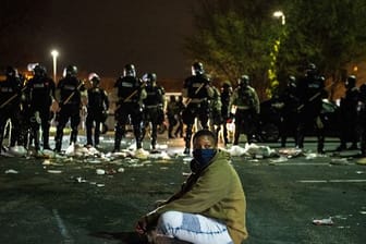 Ein Demonstrant sitzt in Minnesota als Protest auf einer Straße vor einer Reihe von Bereitschaftspolizisten.
