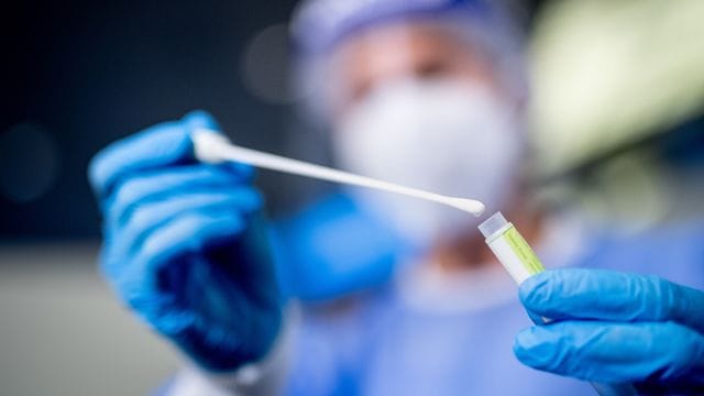 Eine Frau hält am Flughafen München in einem Testcenter die Probe von einem Rachenabstrich in den Händen. Eine Frau hält am Flughafen München in einem Testcenter die Probe von einem Rachenabstrich in den Händen.
