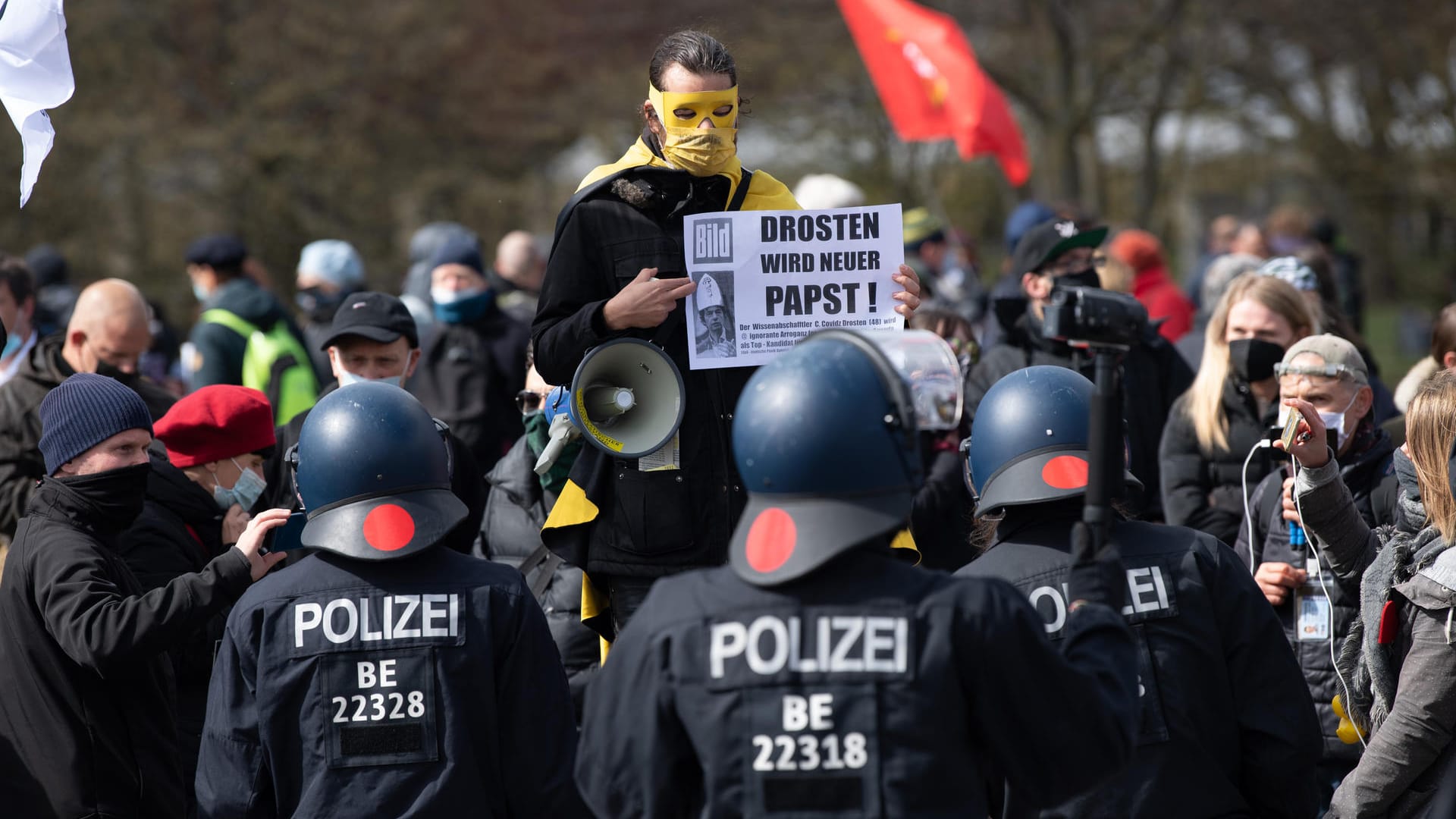 Ein maskierter Demonstrant steht im Regierungsviertel vor Polizeibeamten und hält ein Schild mit der Aufschrift "Drosten wir neuer Papst!" in der Hand: Viele Demonstranten hielten sich nicht an die Corona-Auflagen.