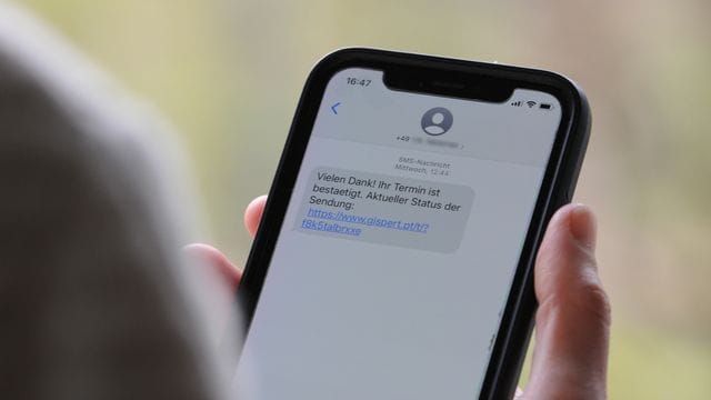 Eine Frau hält ein Smartphone in ihrer Hand, auf dessen Display eine Betrugs-SMS zu lesen ist.