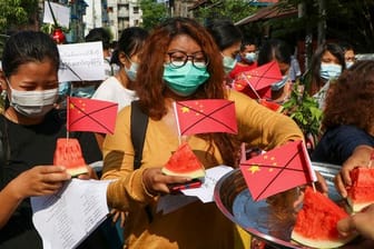 Anti-Putsch-Demonstranten tragen während eines Protests Wassermelonenstücke, in denen durchgestrichene chinesische Fähnchen stecken.