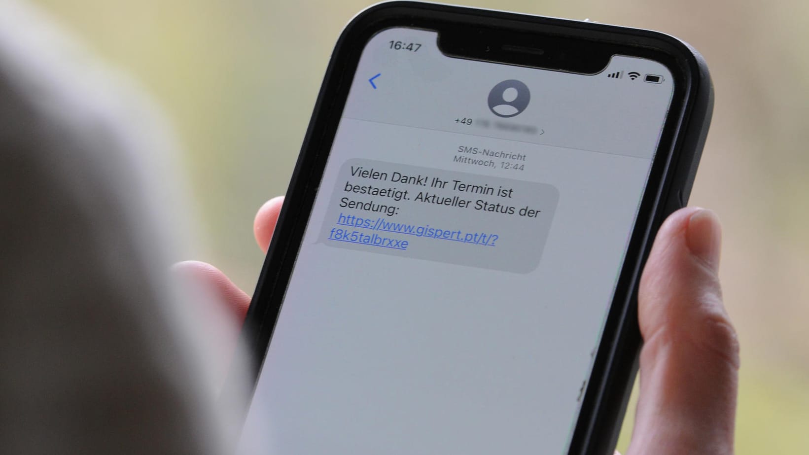 Eine Frau hält ein Smartphone in ihrer Hand, auf dessen Display eine Betrugs-SMS zu lesen ist: Beim sogenannten Smishing setzen Kriminelle darauf, dass Verbraucher auf den mitgeschickten Link klicken und sich in einem nächsten Schritt unwissentlich eine Schadsoftware runterladen.