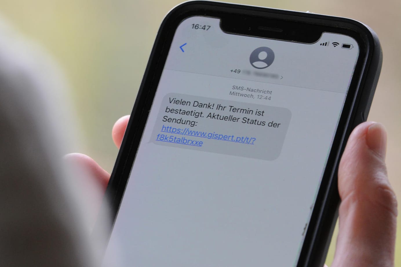 Eine Frau hält ein Smartphone in ihrer Hand, auf dessen Display eine Betrugs-SMS zu lesen ist: Beim sogenannten Smishing setzen Kriminelle darauf, dass Verbraucher auf den mitgeschickten Link klicken und sich in einem nächsten Schritt unwissentlich eine Schadsoftware runterladen.