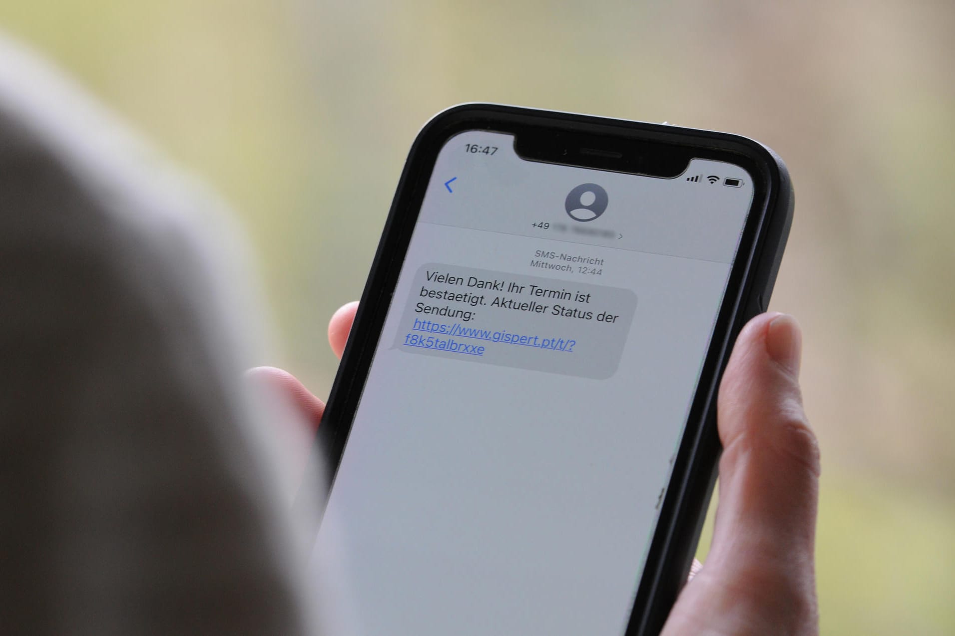 Eine Frau hält ein Smartphone in ihrer Hand, auf dessen Display eine Betrugs-SMS zu lesen ist: Beim sogenannten Smishing setzen Kriminelle darauf, dass Verbraucher auf den mitgeschickten Link klicken und sich in einem nächsten Schritt unwissentlich eine Schadsoftware runterladen.