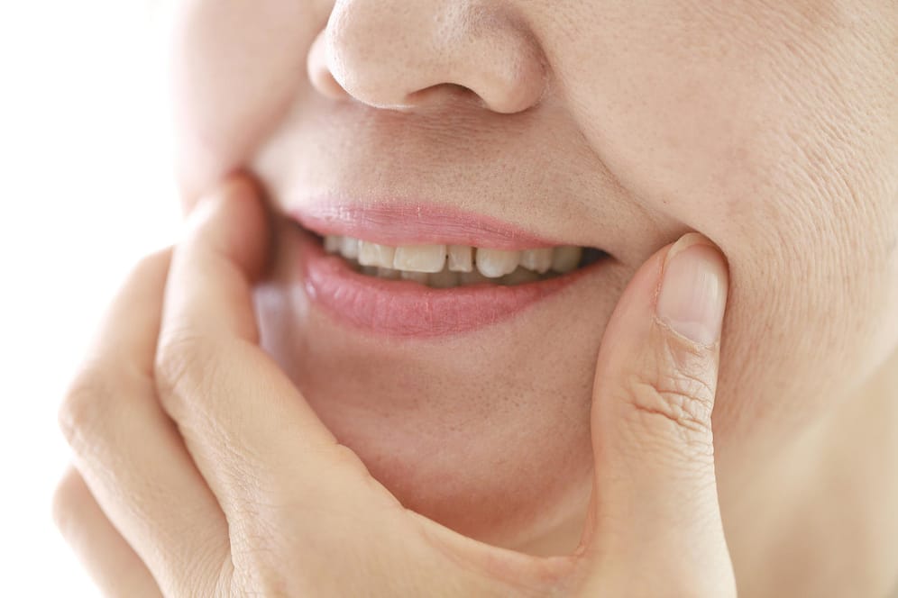Eine Frau zieht die Mundwinkel hoch: Wenn die Haut mit zunehmendem Alter an Elastizität verliert, bilden sich häufig Falten rund um den Mund.
