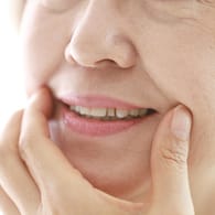 Eine Frau zieht die Mundwinkel hoch: Wenn die Haut mit zunehmendem Alter an Elastizität verliert, bilden sich häufig Falten rund um den Mund.