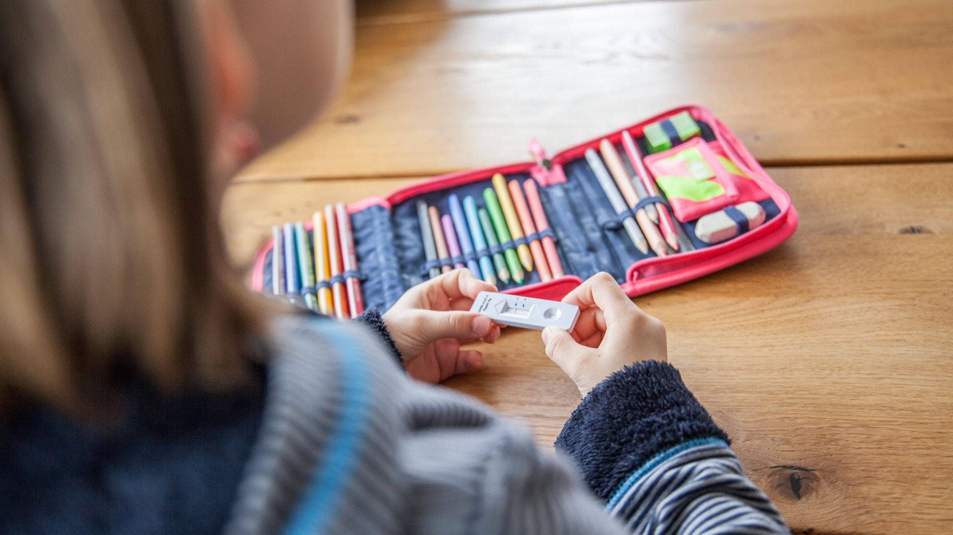 Ein Kind hält einen Antigen-Test in der Hand (Archivbild): In Köln müssen sich Schulkinder vor dem Unterricht auf Corona testen.