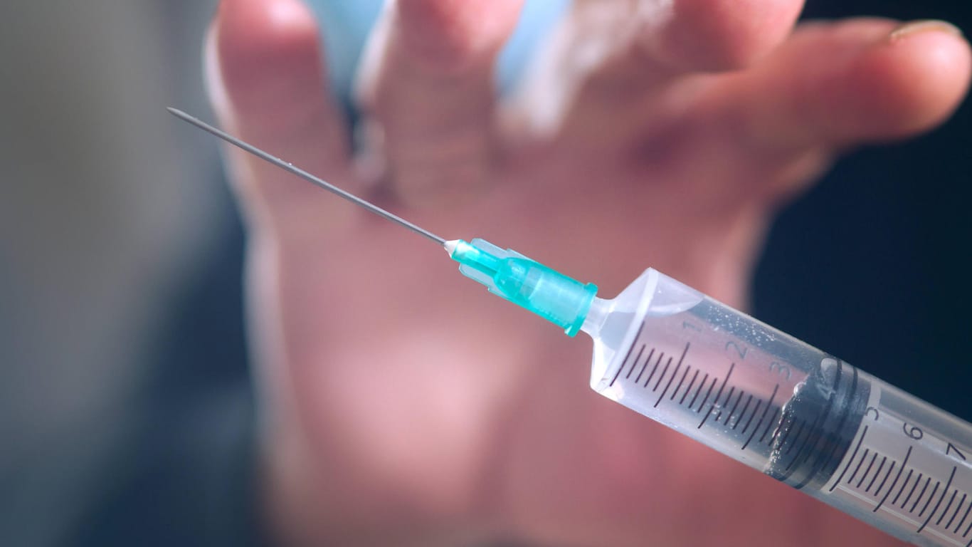 Eine Hand greift nach einer Spritze (Symbolbild): In München wollte ein Mann drei Impfdosen aus dem Impfzentrum stehlen.