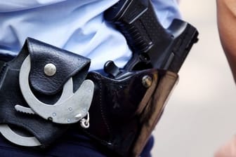Ein Polizist mit Handschellen und Pistole am Gürtel (Archivbild): In Wuppertal haben bis zu 20 Personen etwa Warnbaken auf die Straße geworfen.