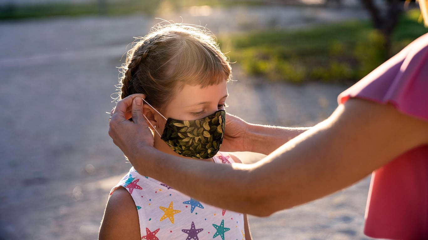 Einem jungen Mädchen wird eine Maske aufgesetzt (Symbolbild): Kinder, die das sechste Lebensjahr noch nicht vollendet haben, müssen in NRW keine Masken tragen.