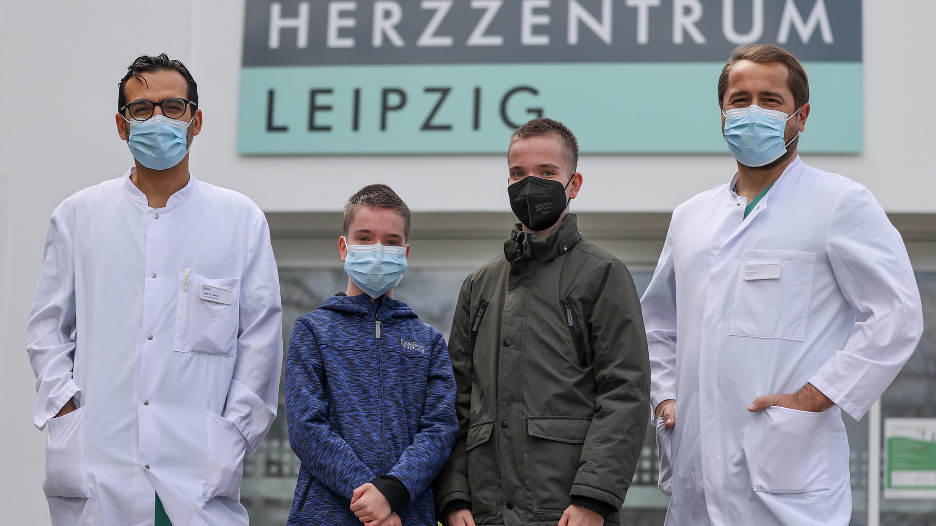 Diyar Saeed (l), Leiter des Herztransplantationsprogramms, Marcel Vollroth (r), Oberarzt Kinderherzchirurgie und die Zwillinge Jamie und Kilian vor dem Herzzentrum Leipzig: Die beiden Ärzte haben den Jungen neue Herzen transplantiert.