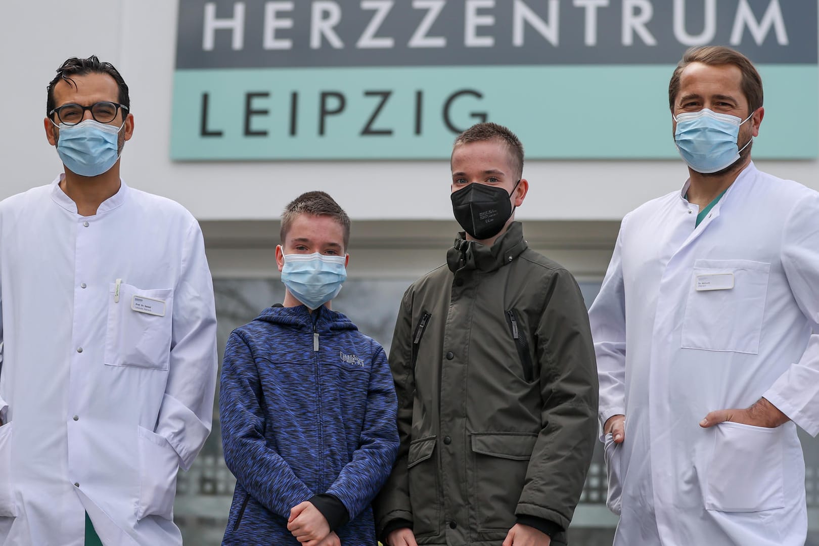 Diyar Saeed (l), Leiter des Herztransplantationsprogramms, Marcel Vollroth (r), Oberarzt Kinderherzchirurgie und die Zwillinge Jamie und Kilian vor dem Herzzentrum Leipzig: Die beiden Ärzte haben den Jungen neue Herzen transplantiert.