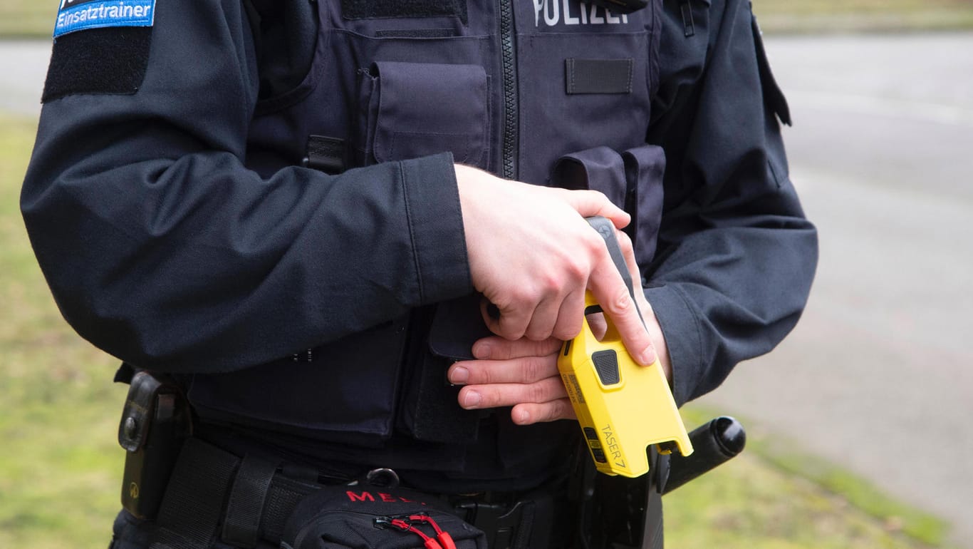 EIn Polizist hält einen Taser in der Hand (Archivbild): Die Grünen fordern das Ende des Pilotprojektes in NRW.