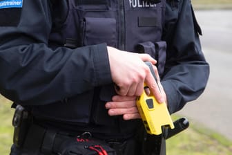 EIn Polizist hält einen Taser in der Hand (Archivbild): Die Grünen fordern das Ende des Pilotprojektes in NRW.