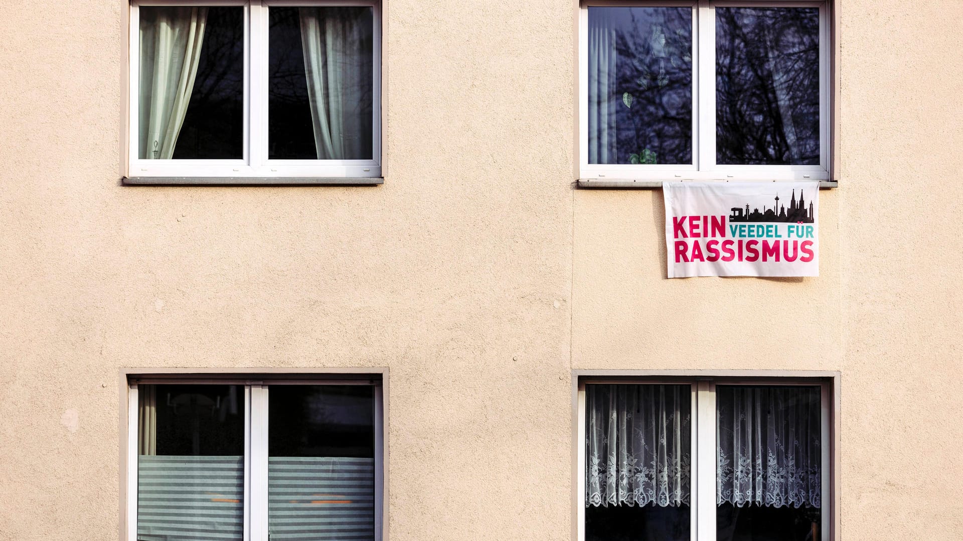 An einem Fenster hängt eine Flagge mit der Aufschrift "Kein Veedel für Rassismus" (Archivbild): Für die Landesregierung stellt die Fahne an Schulen kein Problem dar.