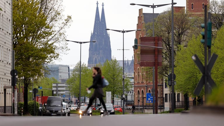 Eine Frau geht über eine Straße, im Hintergrund der Kölner Dom (Symbolbild): Das Leben in der Stadt wird immer noch von der Corona-Pandemie beeinflusst.