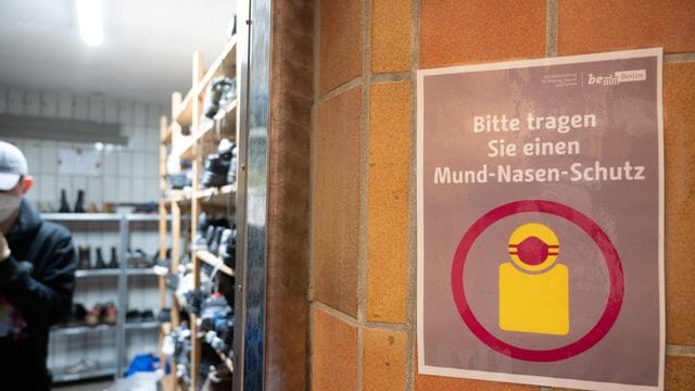 In der Kleiderkammer der Berliner Stadtmission hängt ein Plakat mit der Aufschrift „Bitte tragen Sie einen Mund-Nasen-Schutz“. In der Kleiderkammer der Berliner Stadtmission hängt ein Plakat mit der Aufschrift „Bitte tragen Sie einen Mund-Nasen-Schutz“.