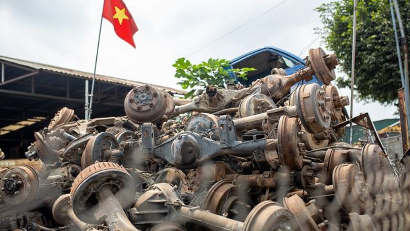 Die Flagge Vietnams weht in Te Lo über einem Haufen rostiger Autoachsen, dahinter steht eine leere LKW-Kabine.