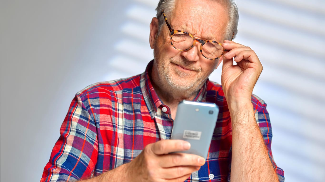 Ein Mann blickt skeptisch auf das Smartphone: Betrüger rufen oft unter falscher Nummer an.