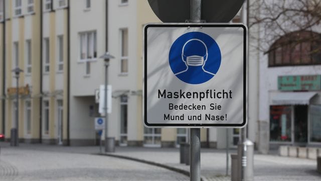 Ein Hinweisschild zur Maskenpflicht steht an der Fußgängerzone. Ein Hinweisschild zur Maskenpflicht steht an der Fußgängerzone.