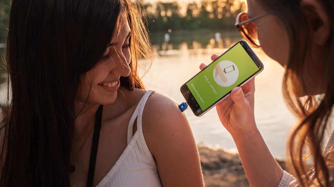 Zwei junge Frauen benutzen "heat it": Der Stecker fürs Smartphone soll gegen juckende Mückenstiche helfen.