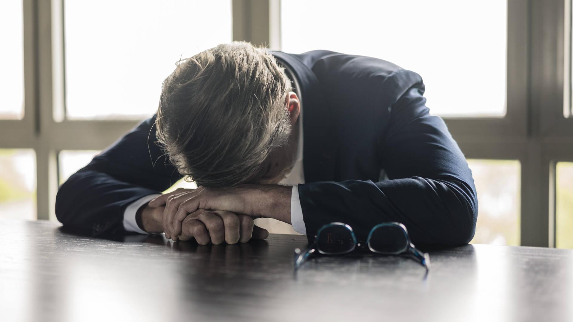 Ein Mann beugt erschöpft über einem Tisch (Symbolbild): Psychische Erkrankungen sind für viele noch immer ein Tabuthema.