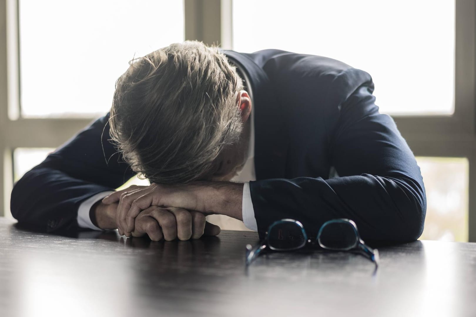 Ein Mann beugt erschöpft über einem Tisch (Symbolbild): Psychische Erkrankungen sind für viele noch immer ein Tabuthema.