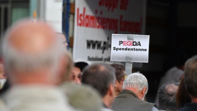 Auf einer Kundgebung von Pegida halten Anhänger ein Schild mit dem Schriftzug "Pegida Spendentonne" in die Höhe. Auf einer Kundgebung von Pegida halten Anhänger ein Schild mit dem Schriftzug "Pegida Spendentonne" in die Höhe.