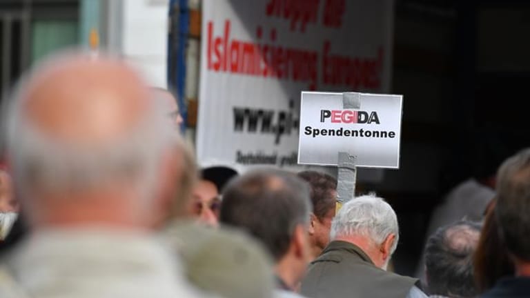Auf einer Kundgebung von Pegida halten Anhänger ein Schild mit dem Schriftzug "Pegida Spendentonne" in die Höhe.