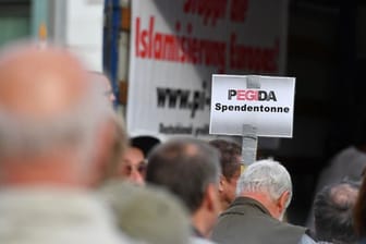Auf einer Kundgebung von Pegida halten Anhänger ein Schild mit dem Schriftzug "Pegida Spendentonne" in die Höhe.