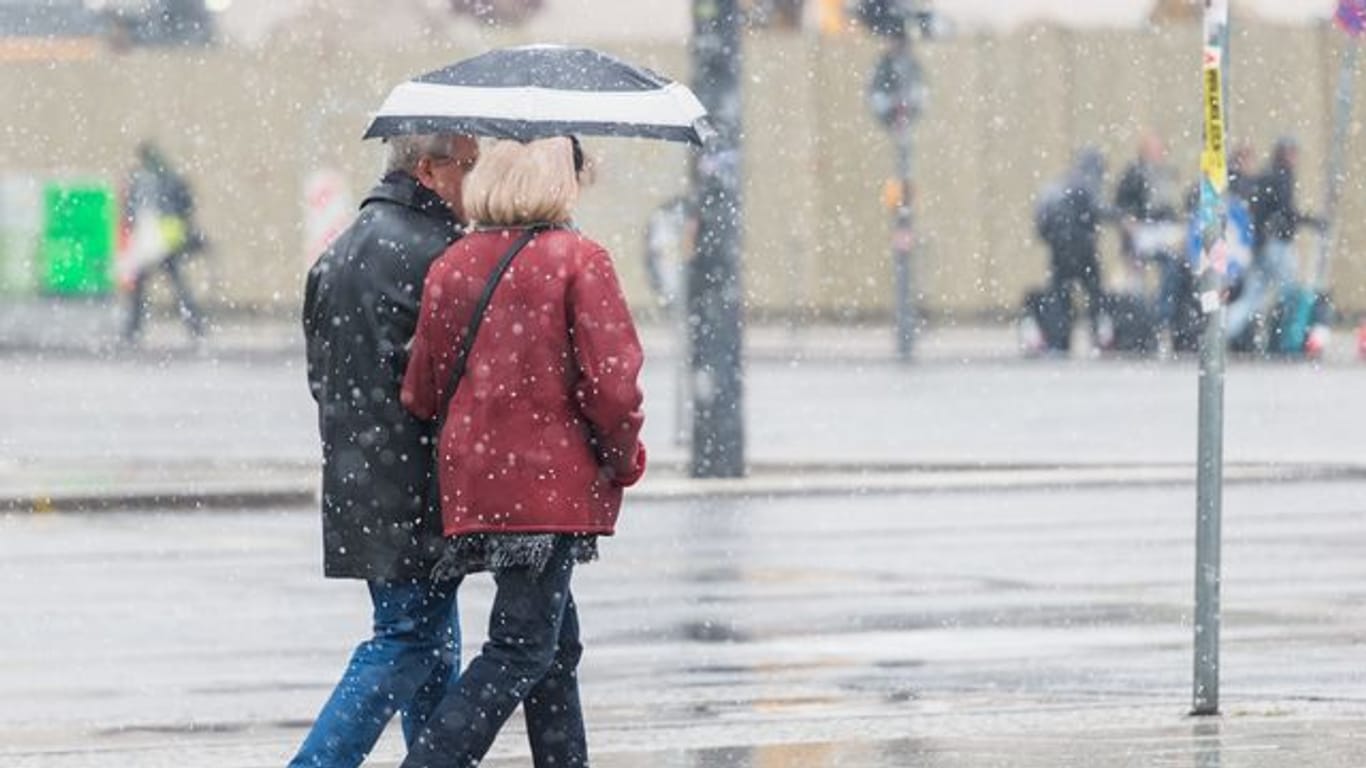 Ein Mann und eine Frau gehen mit einem Regenschirm bei Schneeregen durch Berlin (Archivbild): Ein gen Osten ziehendes Tief bringe sehr feuchte und kalte Luft mit sich.