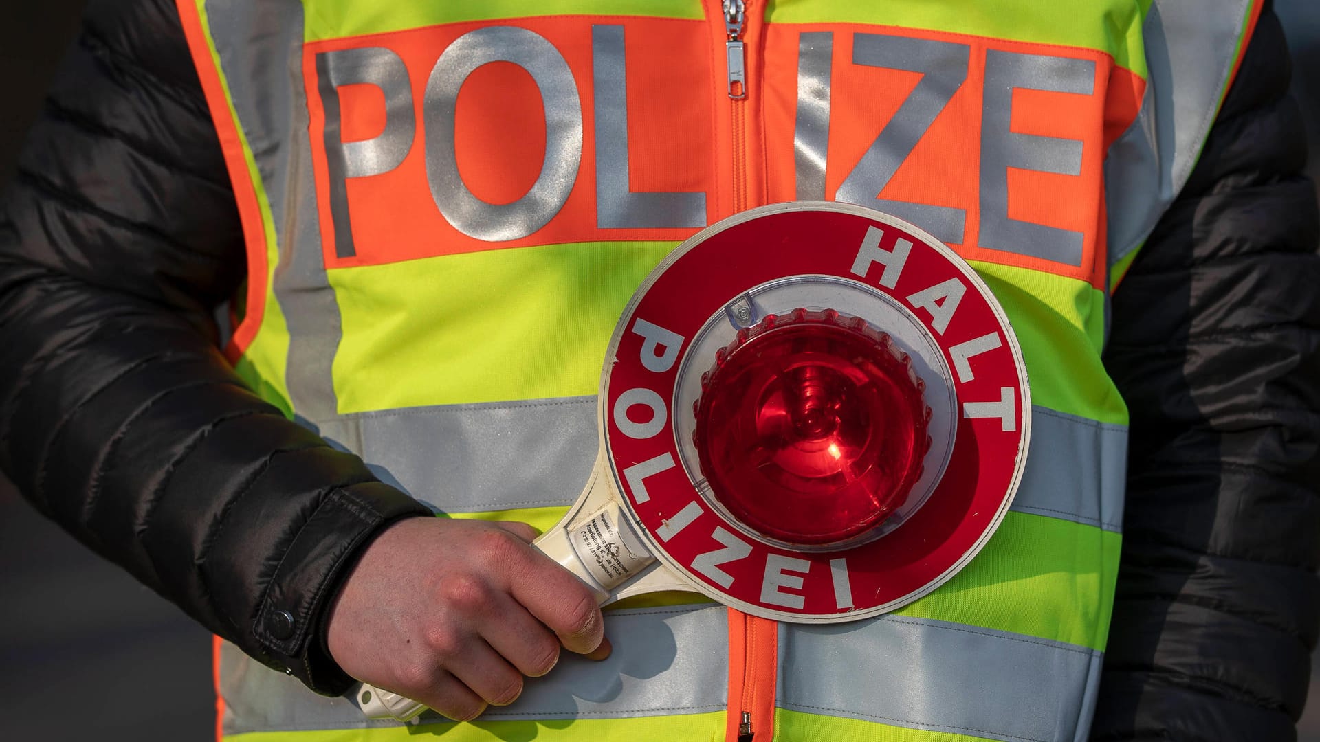 Ein Polizeibeamter hält eine "Stopp"-Kelle in der Hand (Symbolbild): Der Fahrer muss sich nun vor Gericht verantworten.