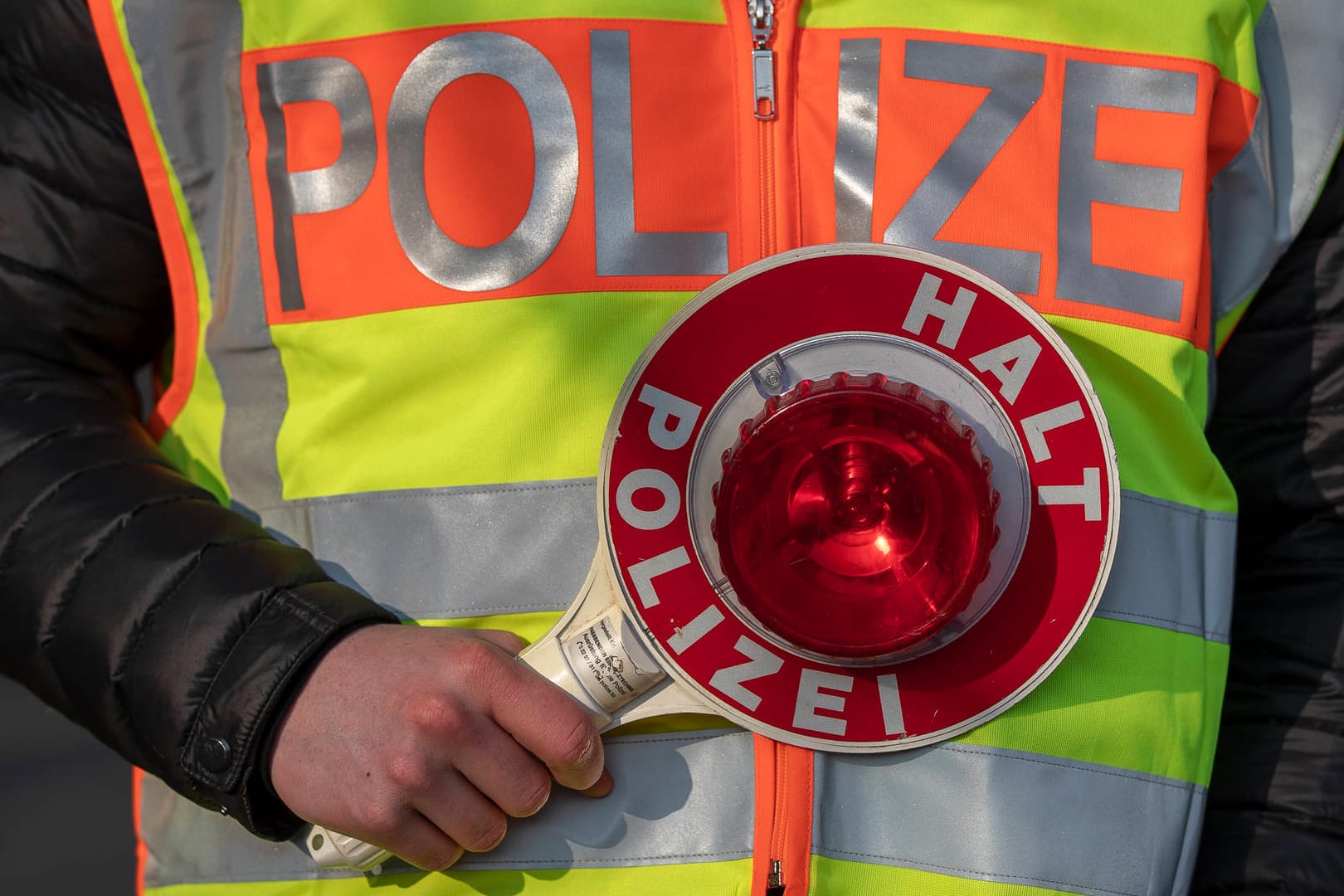 Ein Polizeibeamter hält eine "Stopp"-Kelle in der Hand (Symbolbild): Der Fahrer muss sich nun vor Gericht verantworten.